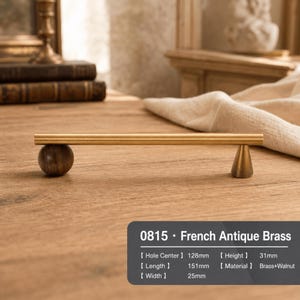 Peut inclure: Une poignée de meuble composée d'une longue barre horizontale en laiton brossé, soutenue par une sphère en noyer foncé d'un côté et un cône en laiton de l'autre. Le texte indique 0815 French Antique Brass, Hole Center 128mm, Height 31mm, Length 151mm, Width 25mm.