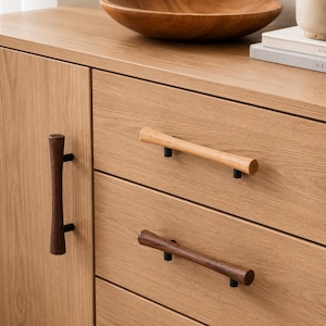 Può includere: Un mobile in legno di rovere chiaro con tre cassetti e un'anta. Il mobile è caratterizzato da maniglie cilindriche in legno in varie tonalità di marrone chiaro e scuro, montate su piccoli supporti in metallo nero a contrasto.
