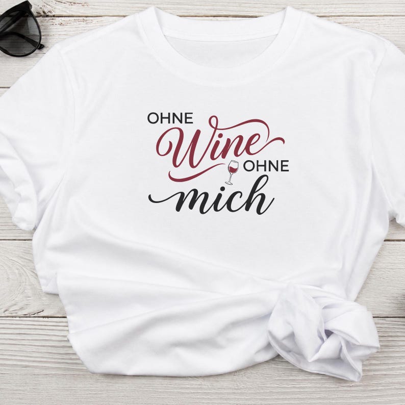 May include: A white short-sleeved t-shirt featuring the black and burgundy text "OHNE Wine OHNE mich" printed on the front. The design includes a small graphic of a wine glass between the words, with "Wine" in a cursive script font.