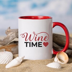 May include: A white ceramic mug with a bright red interior and handle. The front of the mug features the text "Wine" in a red cursive script above the word "TIME" in bold black capital letters, followed by a small red heart symbol.