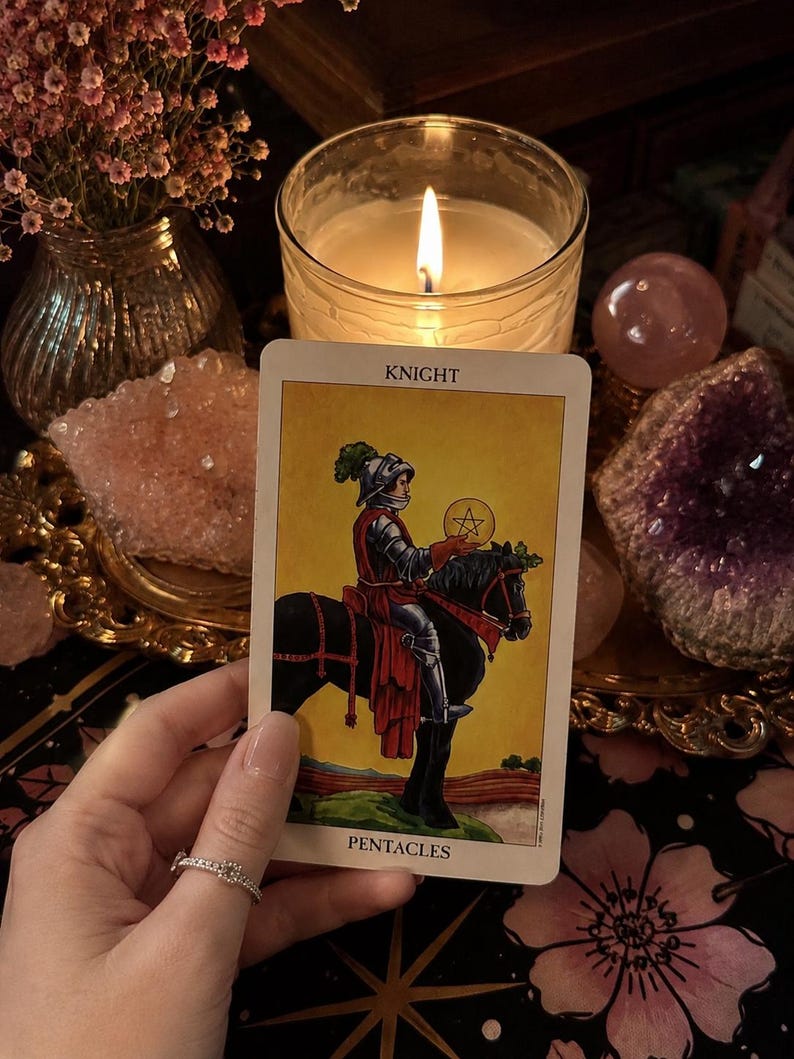 Puede incluir: Una carta de tarot titulada Knight of Pentacles que presenta la ilustraci&oacute;n de un caballero con armadura plateada montando un caballo negro mientras sostiene una moneda de oro con un s&iacute;mbolo de pentagrama. La carta tiene un fondo amarillo.