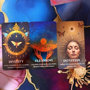 Puede incluir: Tres cartas de or&aacute;culo rectangulares con ilustraciones vibrantes. La primera muestra una mariposa dorada en un c&iacute;rculo con el texto DIVINITY. La segunda muestra manos sosteniendo un sol brillante con el texto CLEANSING. La tercera muestra a una persona con un aura de rayos solares y el texto INTUITION.