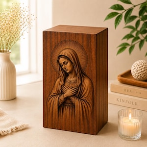 May include: A rectangular wooden urn featuring a laser-engraved image of the Virgin Mary with a halo, depicted with hands crossed over the chest. The dark brown wood grain is visible across the surface of the upright, box-shaped memorial container.