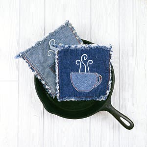 Puede incluir: Dos posavasos de mezclilla azul con bordes deshilachados. Un posavasos tiene un diseño bordado blanco de una taza de café con vapor saliendo de ella.