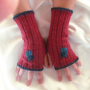 May include: A pair of red fingerless gloves with blue fabric flowers and a dark blue crocheted trim.