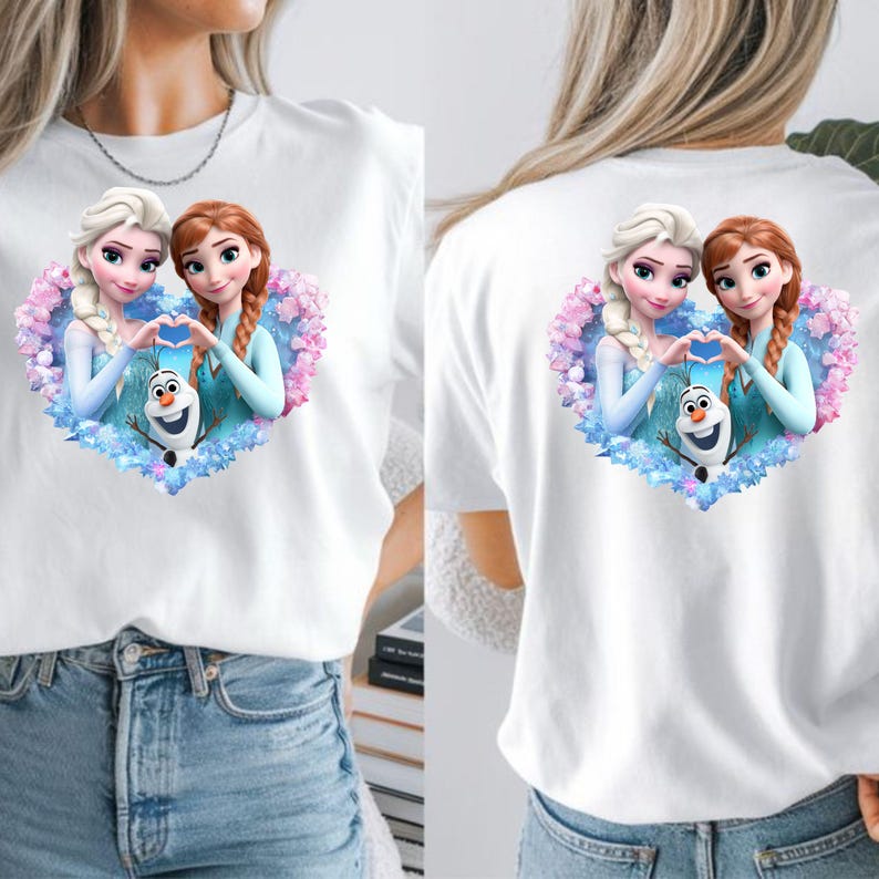 May include: White t-shirt featuring a colorful graphic of two animated princesses forming a heart shape with their hands, with a snowman in the center. The design is surrounded by a heart-shaped floral arrangement. The same design is on the front and back of the shirt.