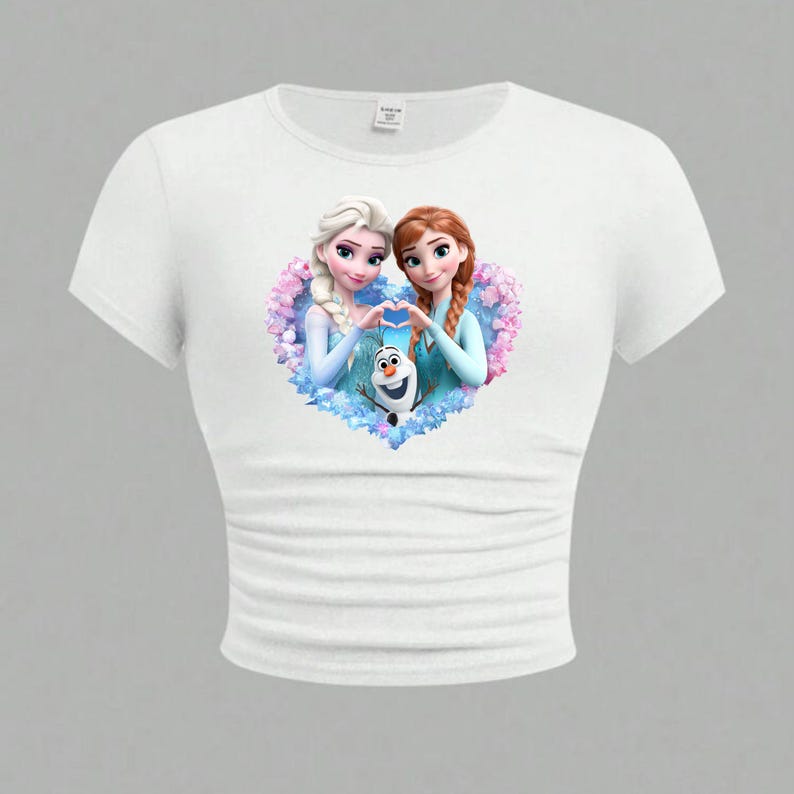 May include: White crop top featuring a colorful graphic of two animated female characters forming a heart shape with their hands, with a snowman in the center. The design is set against a floral background.