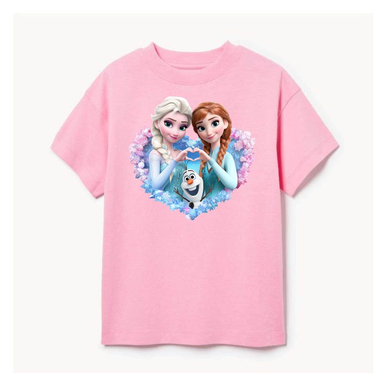May include: A pink t-shirt featuring a heart-shaped graphic with two animated female characters and a snowman. The characters are making a heart shape with their hands. The t-shirt is made of a soft material.