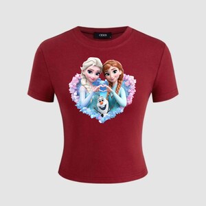 May include: A maroon crop top featuring a graphic of two animated princesses forming a heart shape with their hands, with a snowman in the center. The princesses have blonde and auburn hair. The shirt has short sleeves.