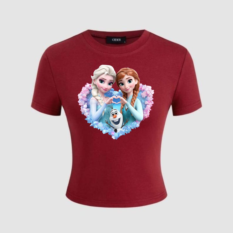 May include: A maroon crop top featuring a graphic of two animated princesses forming a heart shape with their hands, with a snowman in the center. The princesses have blonde and auburn hair. The shirt has short sleeves.