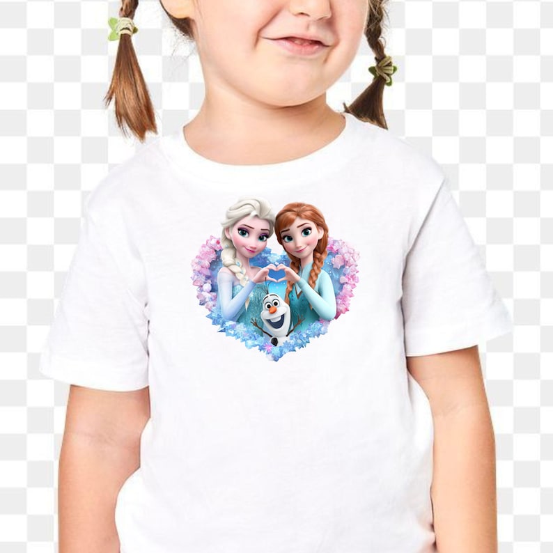 May include: White t-shirt featuring a colorful graphic of two animated princesses forming a heart shape with their hands, with a snowman in the center. The design is set against a floral background.