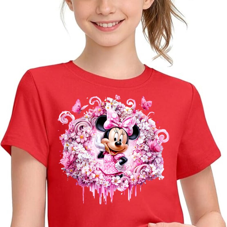 Puede incluir: Una camiseta roja de manga corta con un gr&aacute;fico central de Minnie Mouse con un lazo y un vestido de lunares rosas. Est&aacute; rodeada por un denso arreglo circular de flores rosas y blancas, remolinos y peque&ntilde;as mariposas decorativas.