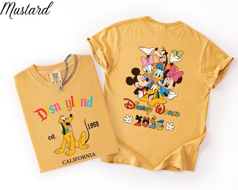May include: Two mustard yellow t-shirts. The left shirt features Pluto, the text Disneyland, est. 1955, and CALIFORNIA. The right shirt displays a group of Disney characters, the text Disney World, and 2026 with Mickey-themed icons.