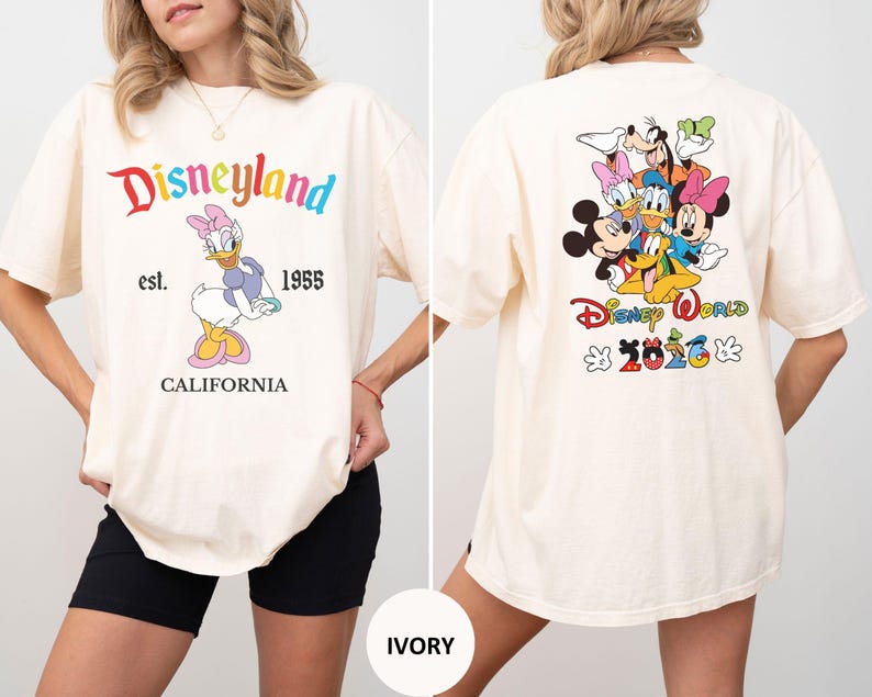 May include: An ivory t-shirt featuring a front graphic of Daisy Duck with the text Disneyland est. 1955 CALIFORNIA. The back graphic displays Mickey Mouse, Minnie Mouse, Donald Duck, Daisy Duck, Goofy, and Pluto with the text Disney World 2026.