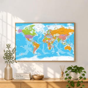 May include: A rectangular wall map of the world featuring a vibrant colour-coded political design on a bright blue ocean background. The map displays continents, countries, and major geographical labels in black text, framed in a thin wooden border.