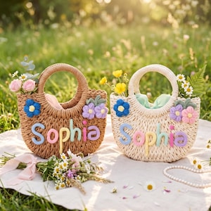 May include: Two round straw handbags, one tan and one cream, each featuring the name Sophia in colourful yarn lettering. Both bags are decorated with crocheted blue, purple, and pink flowers and contain small bouquets of fresh flowers.
