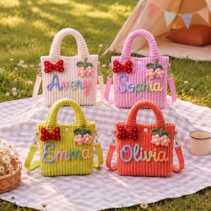 May include: Four corduroy tote bags in light pink, bright pink, lime green, and orange. Each bag features a red polka-dot bow, a small crocheted flower cluster, and a personalized name in colorful raised lettering with a detachable shoulder strap.