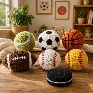 Puede incluir: Una colección de siete pelotas deportivas tejidas a ganchillo que incluye una pelota de tenis verde, un balón de fútbol blanco y negro, un balón de baloncesto naranja, un balón de fútbol americano marrón, una pelota de béisbol blanca, una de sóftbol amarilla y un disco de hockey negro plano con borde blanco.