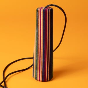 May include: A cylindrical pendant crafted from vertically layered, multi-coloured wood strips in shades of blue, pink, green, and natural wood tones. A thin black braided cord is attached to the top centre, extending downwards on both sides.