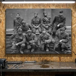 May include: Black and white photograph of a group of uniformed soldiers. The soldiers are wearing military uniforms and caps. Some are seated, while others are standing. The photograph is mounted on a wooden surface.
