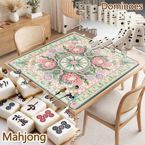 May include: A square table mat featuring a central compass rose surrounded by pink protea flowers, green foliage, and seashells on a light background. The mat is placed on a wooden table with white mahjong tiles and dominoes visible nearby.