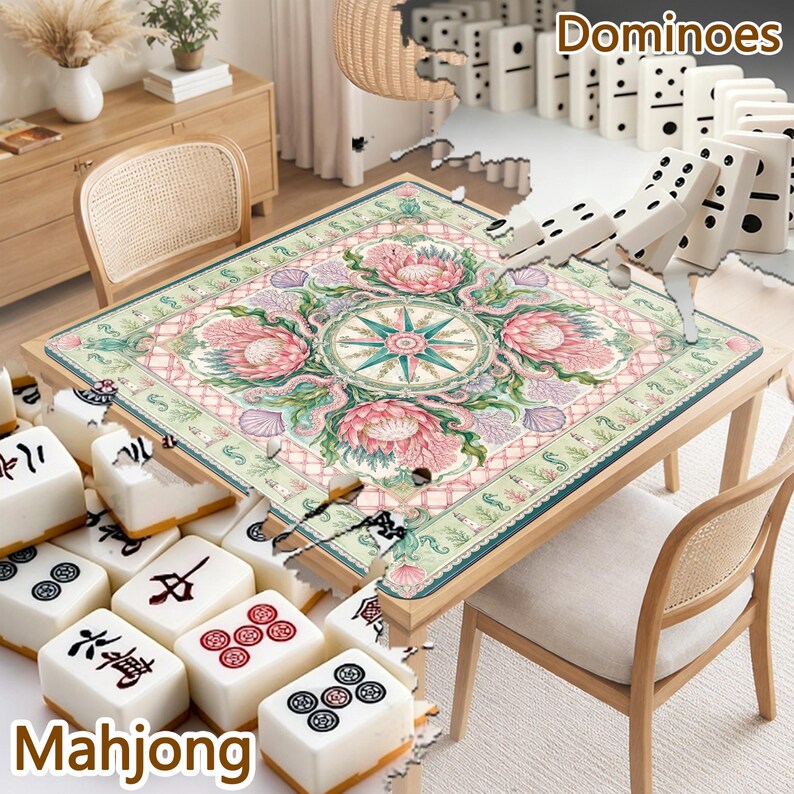 May include: A square table mat featuring a central compass rose surrounded by pink protea flowers, green foliage, and seashells on a light background. The mat is placed on a wooden table with white mahjong tiles and dominoes visible nearby.