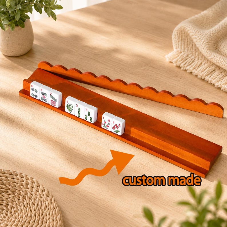 May include: A long, rectangular wooden mahjong tile rack with a scalloped top edge and a grooved ledge for holding tiles. Several white mahjong tiles with red, green, and black symbols are arranged on the rack. The text custom made is visible.