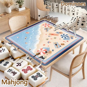 May include: A square table featuring a beach-themed mat with illustrations of people, umbrellas, and towels on sand and water. The table is surrounded by white mahjong tiles with black and red symbols and a set of white dominoes with black dots.