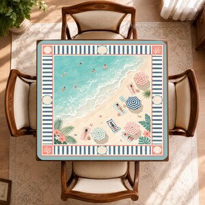 May include: A square table cover featuring a beach scene with turquoise water, white waves, and tan sand. The design includes people on towels, colorful striped umbrellas, palm leaves, and hibiscus flowers, framed by a blue and white striped border.
