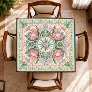May include: A square table cover featuring a central compass rose surrounded by four large pink protea flowers, coral, and seashells. The border displays a repeating pattern of lighthouses and seahorses on a light green background.