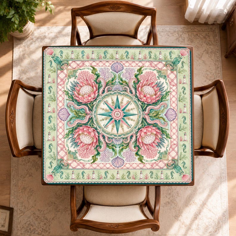 May include: A square table cover featuring a central compass rose surrounded by four large pink protea flowers, coral, and seashells. The border displays a repeating pattern of lighthouses and seahorses on a light green background.
