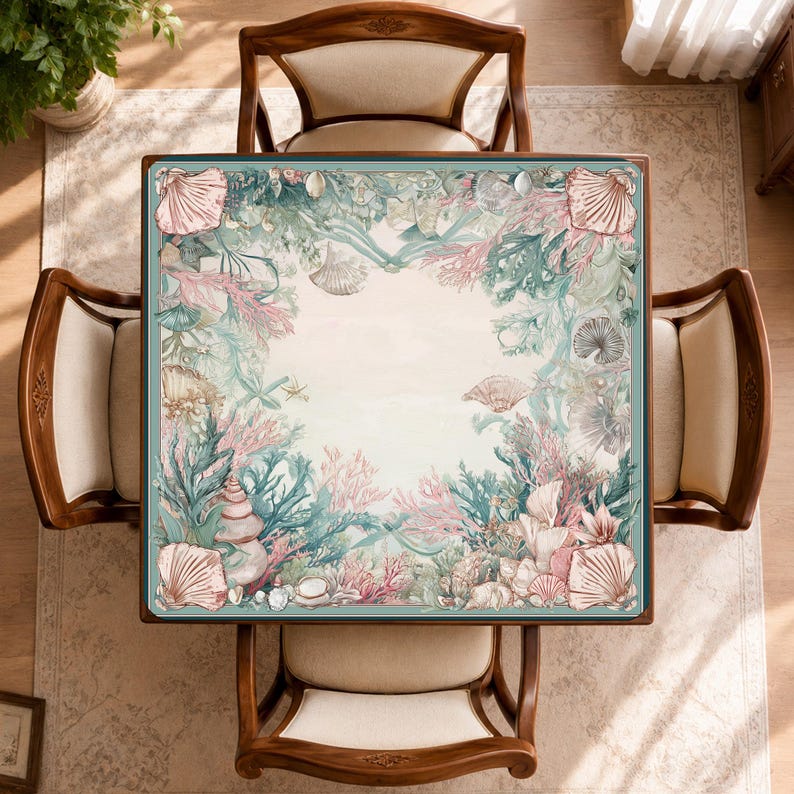 May include: A square table cover featuring a border of intricate illustrations of seashells, coral reefs, and aquatic plants in shades of soft pink, teal, and cream. The center of the fabric is a solid cream color, framed by the detailed marine life pattern.