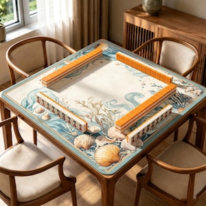 Op de afbeelding: Een vierkante houten mahjongtafel met een maritiem thema, met schelpen en oceaangolven. De tafel is omringd door vier houten stoelen. Oranje en witte mahjongtegels zijn op het tafeloppervlak geplaatst.