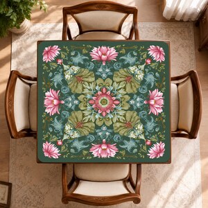May include: A square table cover featuring a dark green background with a symmetrical floral pattern. The design includes large pink lotus flowers, intricate light green foliage, and decorative swirls arranged in a repeating motif.