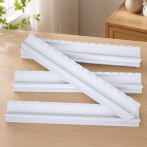 Puede incluir: Un conjunto de cuatro soportes para fichas de juego de pl&aacute;stico blanco, cada uno con un canal horizontal largo para sostener fichas y un borde superior festoneado. Los soportes est&aacute;n dispuestos en una formaci&oacute;n apilada, mostrando su forma uniforme.