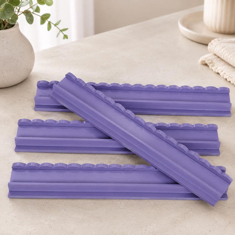 Puede incluir: Cuatro tiras de silicona de color morado con un borde superior festoneado y una base plana. Cada tira presenta un canal largo y estrecho que recorre horizontalmente el centro, con una textura suave y un color morado uniforme y vibrante.