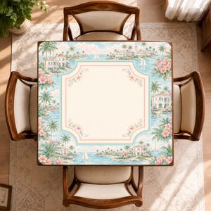May include: A square table with a light cream center and a decorative border featuring a tropical coastal scene with palm trees, sailboats, villas, and pink flowers. The table is surrounded by four wooden chairs with cream-colored upholstered seats.