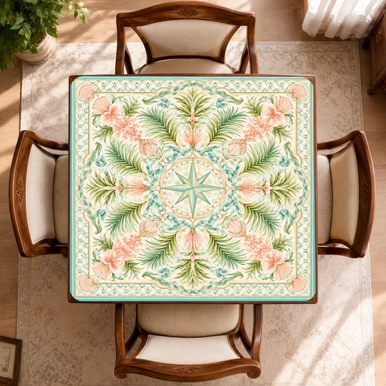 May include: A square tablecloth featuring a central compass rose motif surrounded by a symmetrical pattern of green palm fronds, pink hibiscus flowers, and seashells. The design is framed by a decorative border in shades of teal and cream.