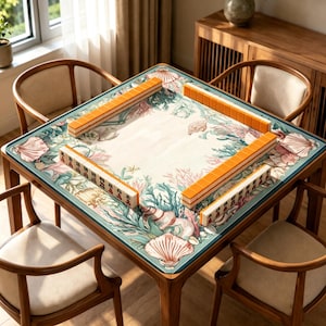 May include: A square mahjong table featuring a play mat with a printed design of seashells, coral, and seaweed in shades of pink, green, and teal. The table is set with four rows of orange-backed mahjong tiles arranged in a square formation.