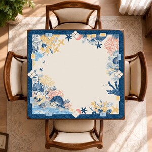 May include: Overhead view of a square table with a cream-colored surface and a navy blue border. The border is decorated with a marine-themed design featuring coral, seashells, and starfish in shades of blue, yellow, and pink. Four wooden chairs surround the table.