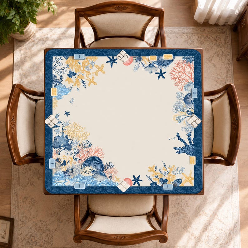May include: Overhead view of a square table with a cream-colored surface and a navy blue border. The border is decorated with a marine-themed design featuring coral, seashells, and starfish in shades of blue, yellow, and pink. Four wooden chairs surround the table.