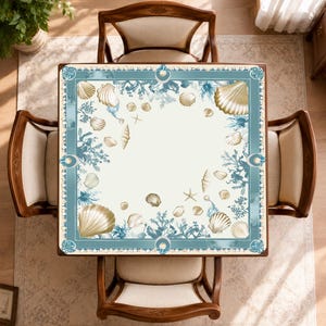 Peut inclure: Vue a&eacute;rienne d'une table carr&eacute;e orn&eacute;e de coquillages. Quatre chaises en bois avec coussins beiges l'entourent. La table pr&eacute;sente un fond cr&egrave;me avec une bordure bleue et dor&eacute;e orn&eacute;e de coquillages et de coraux.