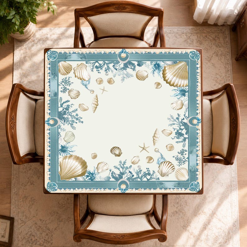 Peut inclure: Vue a&eacute;rienne d'une table carr&eacute;e orn&eacute;e de coquillages. Quatre chaises en bois avec coussins beiges l'entourent. La table pr&eacute;sente un fond cr&egrave;me avec une bordure bleue et dor&eacute;e orn&eacute;e de coquillages et de coraux.