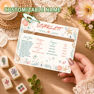 Pode incluir: Um cartão de referência retangular para Mahjong com o nome SCARLETT impresso em vermelho. O cartão apresenta regras para Joker, Charleston, Dragões e Sets, decorado com conchas, pérolas e peças de Mahjong num fundo branco.