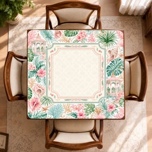 May include: A square table featuring a central cream-colored panel with a subtle geometric pattern, surrounded by a decorative border of pink gazebos, tropical green palm leaves, vibrant pink hibiscus flowers, seashells, and coral reefs.