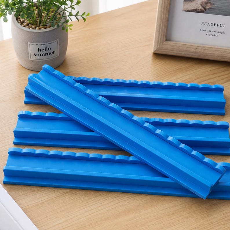 Puede incluir: Un conjunto de cuatro organizadores rectangulares de pl&aacute;stico azul brillante, con un borde superior festoneado y un canal empotrado. Cada pieza tiene una base plana y un lado elevado con textura ondulada para sostener objetos en l&iacute;nea.