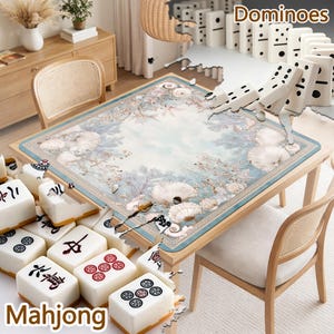 May include: A square table mat featuring a light blue and white coastal design with seashells and coral patterns, surrounded by white mahjong tiles with black and red symbols and white dominoes with black dots arranged on the table surface.