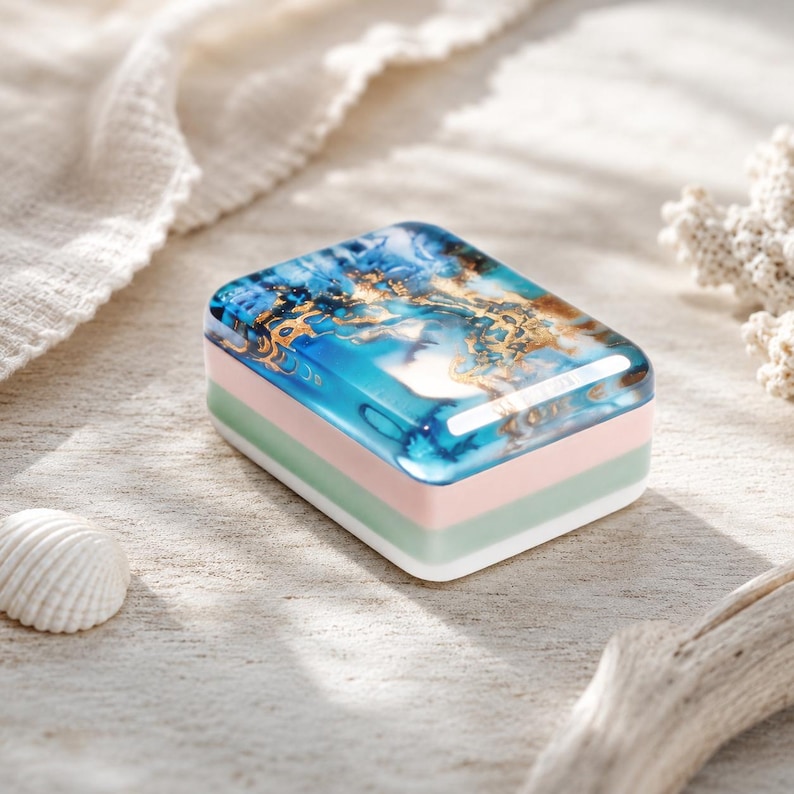 May include: A rectangular soap bar featuring a glossy top layer with a marbled pattern of deep blue, turquoise, and metallic gold swirls. The base consists of three distinct stacked layers in solid white, pale sage green, and soft pastel pink.