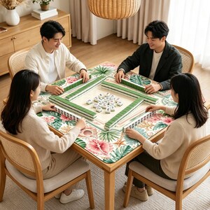 May include: A square wooden table featuring a mahjong set with green tiles and a central pile of white tiles. The table surface is covered by a mat decorated with a colorful tropical floral and seashell pattern in shades of pink and green.
