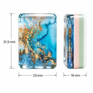May include: Two rectangular resin blocks with rounded corners. The left block features a blue and gold marbled pattern, measuring 31.5 mm in height and 23 mm in width. The right block shows a side profile with blue, pink, and green layers, 16 mm wide.